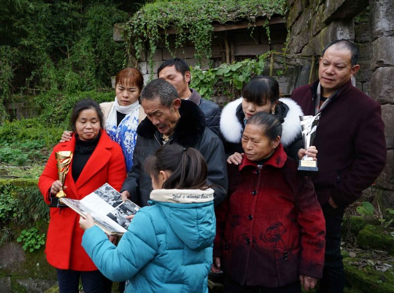 图五：2019年2月，黄光学一家与两个女儿及四女婿，在1951年6月土改时分得的瓦房前合影。老瓦房快拆完了，还剩下几面石墙。黄老一边拿着时盘棋老师后来寄给他的摄影画册，一边给小孙女黄琳琳介绍当年穷苦的情景。（柳代朋 摄）