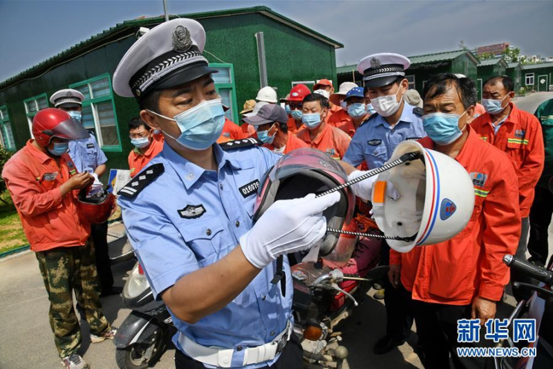 6月9日，青岛高新区交警大队民警给工人讲解工程安全帽为何不能替代头盔使用。新华社记者 李紫恒摄