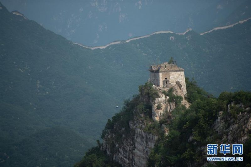 工人在箭扣长城一处敌楼上使用索道运输物资(6月11日摄)。 一根木棍、一部相机,烈日下,64岁的长城修缮师程永茂爬上了有400多年历史的箭扣长城,多年来的自然侵蚀和人为破坏使这段长城残损严重。从最低点“箭扣关”开始,踏过坑洼的城砖、翻过高耸的山崖,一路向东南1000多米,直至海拔990米高的敌楼“正北楼”,这是程永茂的行进路线。 北京市怀柔区箭扣长城东段修缮工程总长度1094米,北京怀建集团有限公司工程师程永茂承担着技术指导工作。对16年来共修缮长城近20000米的他来说,这一段长城最险,“几乎整段都在悬崖峭壁上,坡度有七八十度”。要登上长城,不得不手脚并用着攀爬。年逾花甲的程永茂坚持每周至少上一次长城检查工作,腿脚比一些年轻人还利索。长城上哪里陡峭、哪里残损都深深印在他的脑子里。 “最小干预”,保护长城的完整性、真实性、安全性是程永茂把握的修缮原则。遵循着原始修缮工艺,他总结出随层、随坡、随弯、随旧、随残的“五随”法,从而保持长城的古朴风貌,把正确的长城文化信息留给后人。 新华社发(陈钟昊摄)