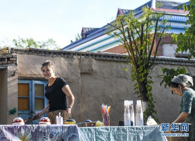 7月4日，在位于六星街内的一家民居前，房主麦尔比岩·艾买提江（左）和母亲在售卖自家制作的酸奶。 新华社记者 王菲 摄