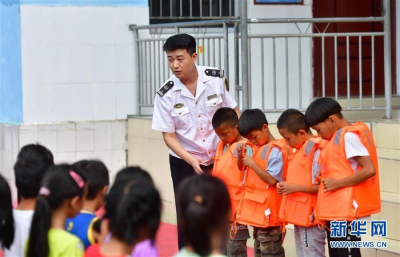 7月13日，在广西融水苗族自治县杆洞乡党鸠小学，融水海事处工作人员指导学生穿救生衣。 当日，广西柳州融水海事处在杆洞乡党鸠小学开展防溺水及水上交通安全知识教育活动，向学生们普及水上安全知识，并讲解水上应急救援技能。 新华社记者 黄孝邦 摄