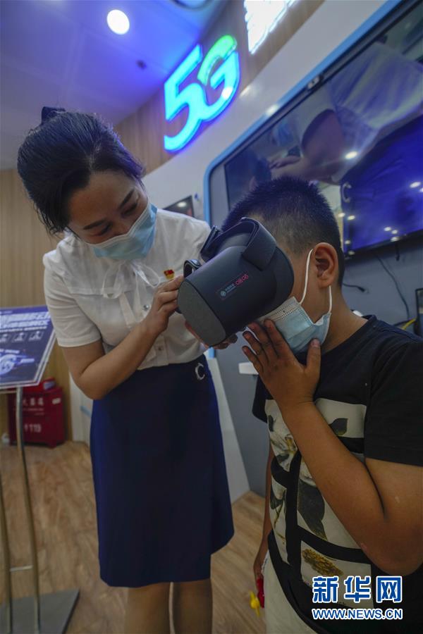 在中国移动位于乌鲁木齐市新市区北京路的一家营业厅，经理张莉向一名小朋友介绍基于5G技术的VR眼镜（7月3日摄）。新华社记者 赵戈 摄