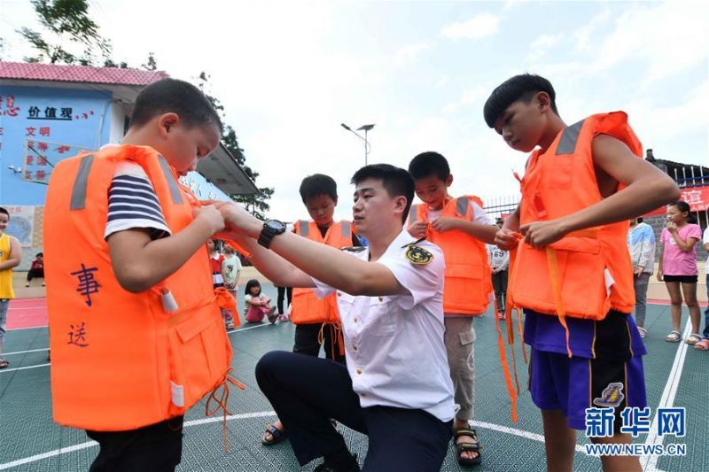 7月13日，在广西融水苗族自治县杆洞乡党鸠小学，融水海事处工作人员指导学生穿救生衣。 当日，广西柳州融水海事处在杆洞乡党鸠小学开展防溺水及水上交通安全知识教育活动，向学生们普及水上安全知识，并讲解水上应急救援技能。 新华社记者 黄孝邦 摄1