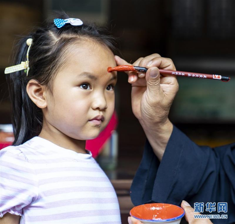 6月24日，在湖北省宜昌市秭归县屈原故里景区端午习俗馆，一名老人为孩子点雄黄酒。 端午佳节将至，各地群众举行了多种多样的活动迎接这一传统节日。 新华社发（向红梅 摄）