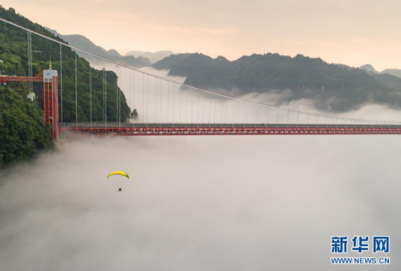 6月26日，在湖南省吉首市，游客乘坐动力伞在矮寨特大悬索桥附近飞翔。 当日是端午小长假的第二天，人们外出休闲，亲近自然，欢度假期。 新华社发（张术杰 摄）